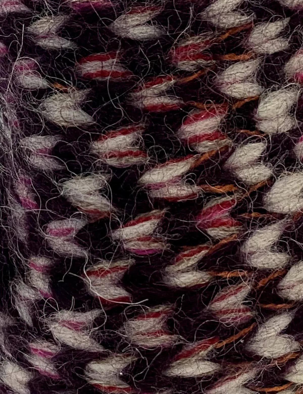 Close-up of the stitch on a knitted mitten, in marled rose and burgundy yarn.