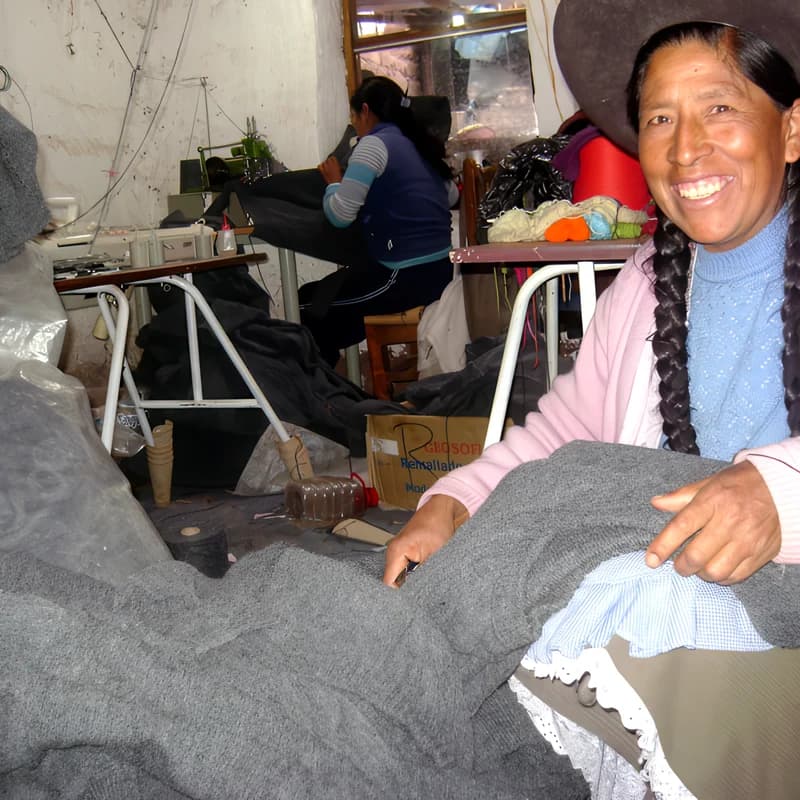Tejedora del taller sonriendo, revisando una prenda.
